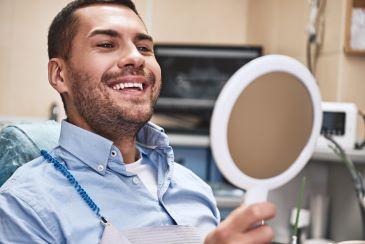 Man looking at teeth in handheld mirror after gum treatment, nashville tn