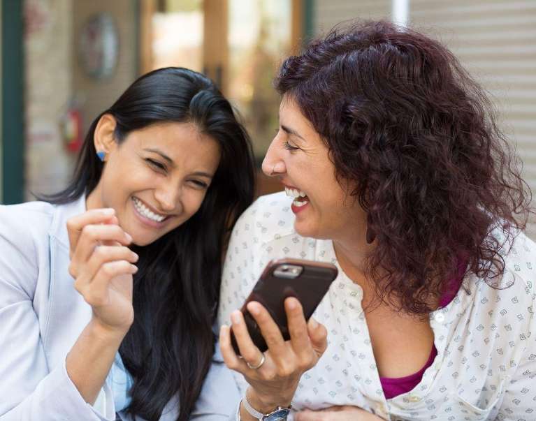Women smiling together looking at phone after indidvidual dental implants, nashville tn