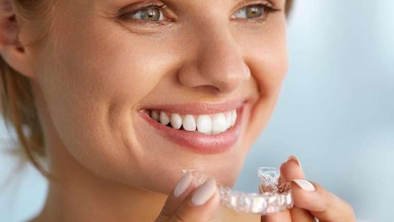 Woman smiling and holding invisalign aligner, brentwood tn